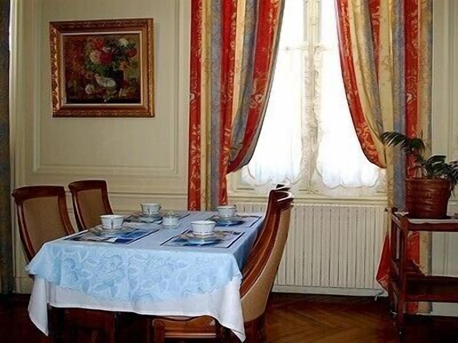 A dining room with a table set for four, a framed painting on the wall, and a window with striped curtains.