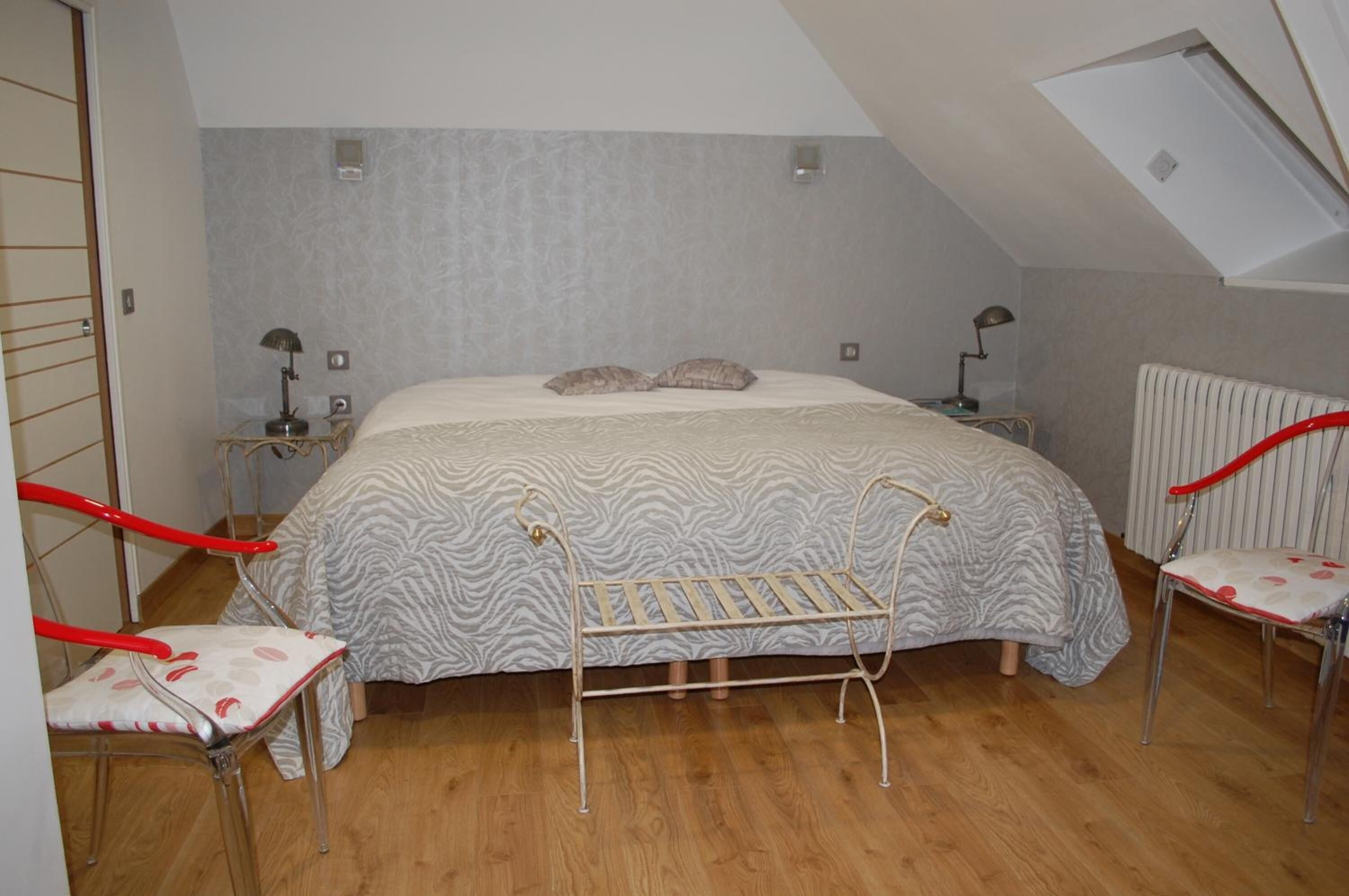 A bedroom with a bed, two nightstands, a radiator, a bench, and two chairs.