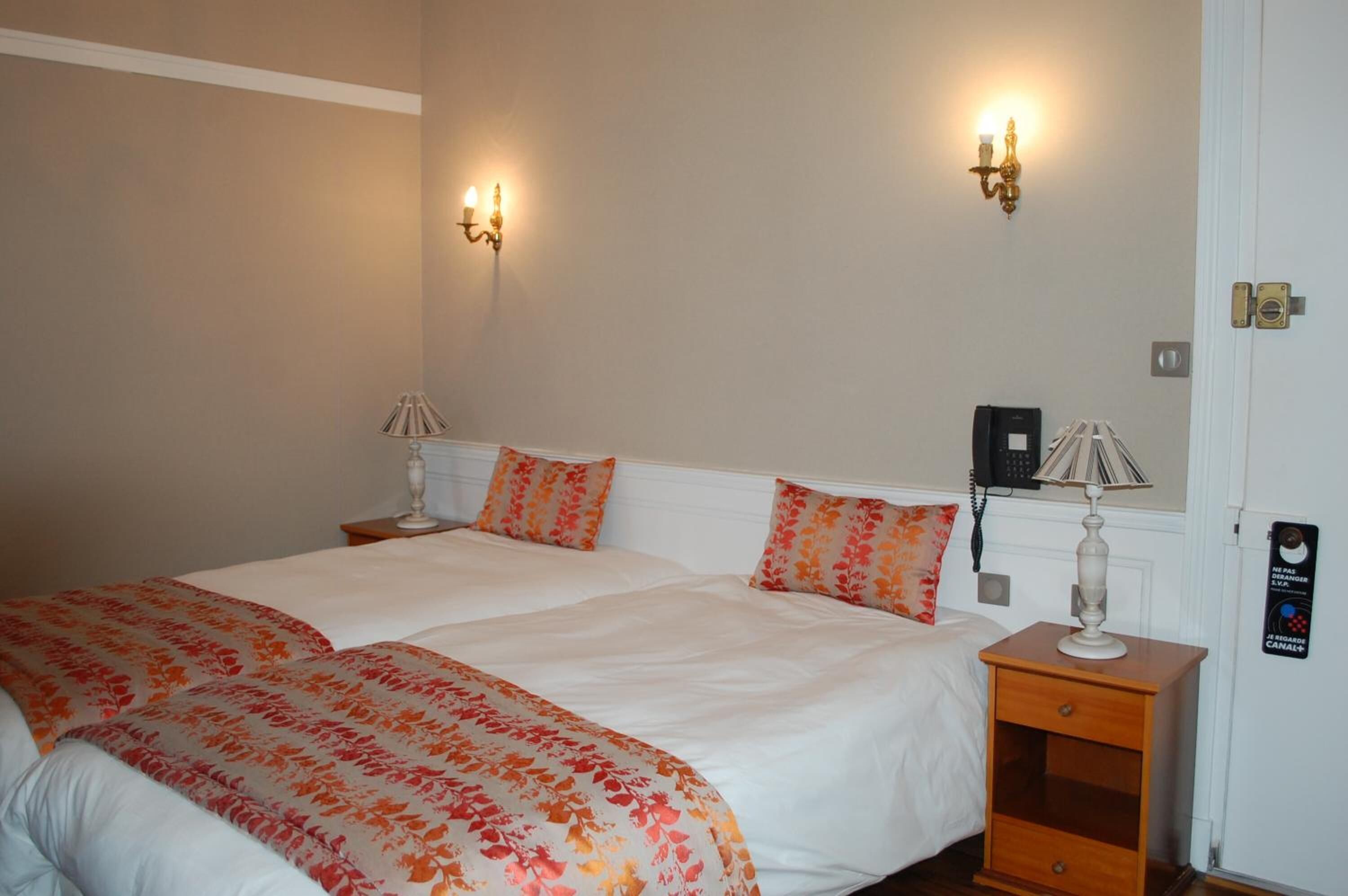 A double bed with floral bedding, two wall-mounted lamps, a bedside table with a lamp, and a door with a lock.