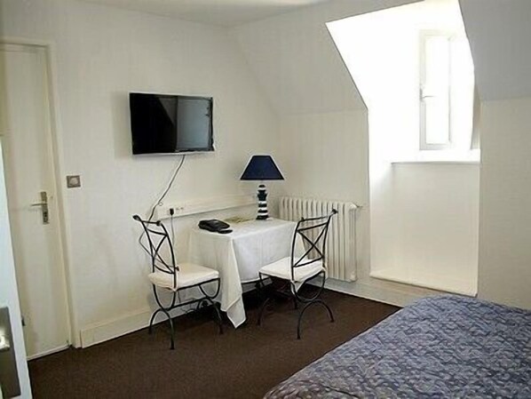 A small, single-room hotel room with a bed, a desk with a chair, a television, and a window.