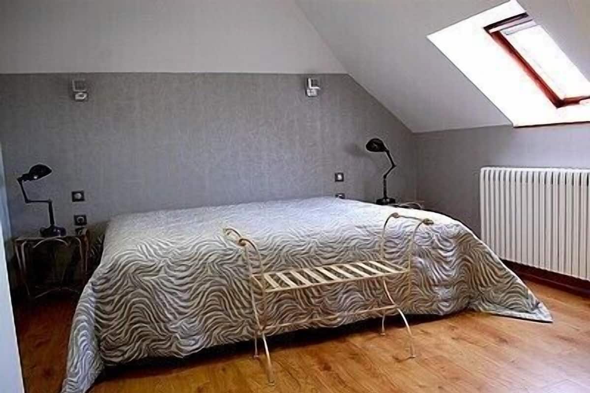 A small, single-bed room with a sloped ceiling and a skylight. There is a radiator on the wall and two bedside lamps.