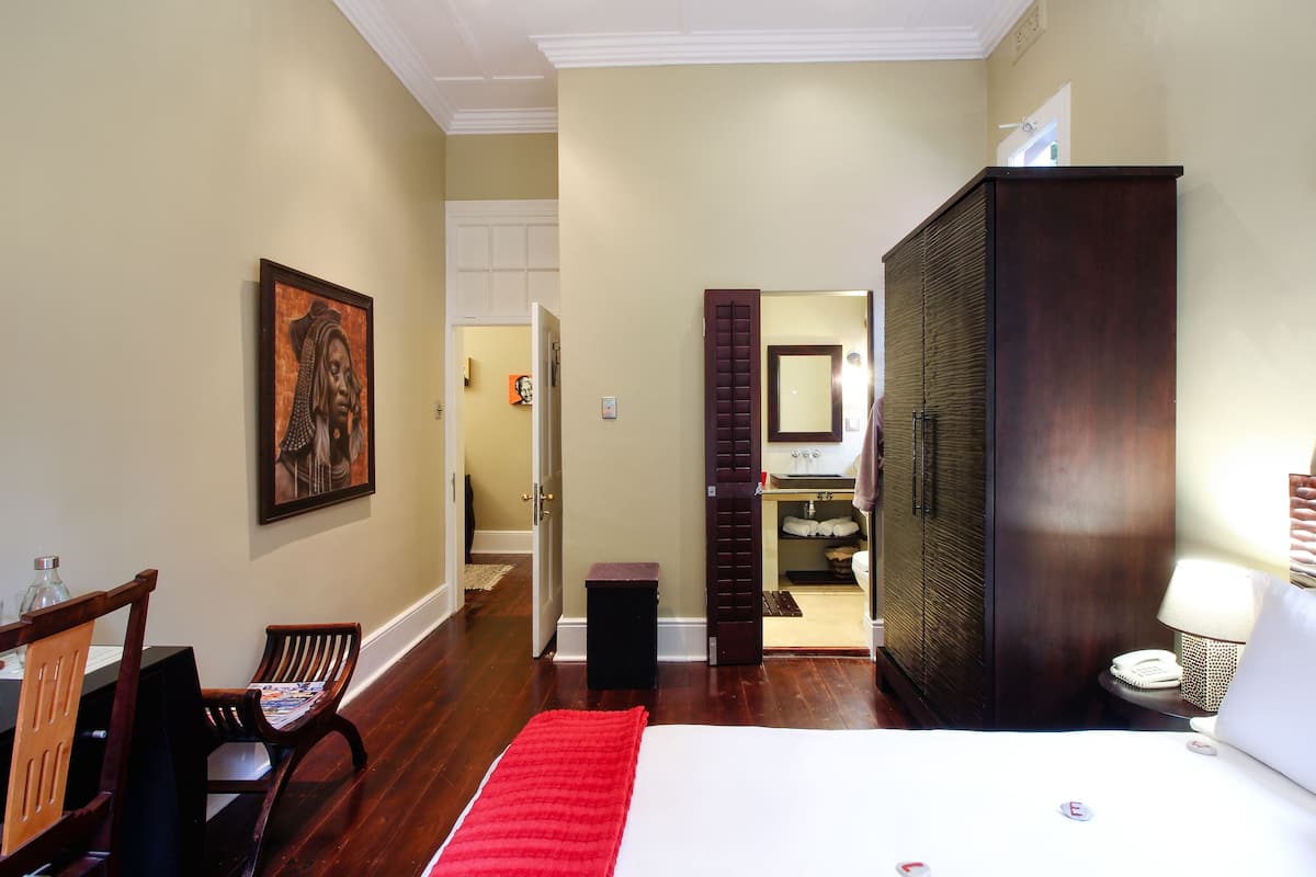 A hotel room with a bed, a desk, a chair, a wardrobe, and a bathroom visible through an open door.