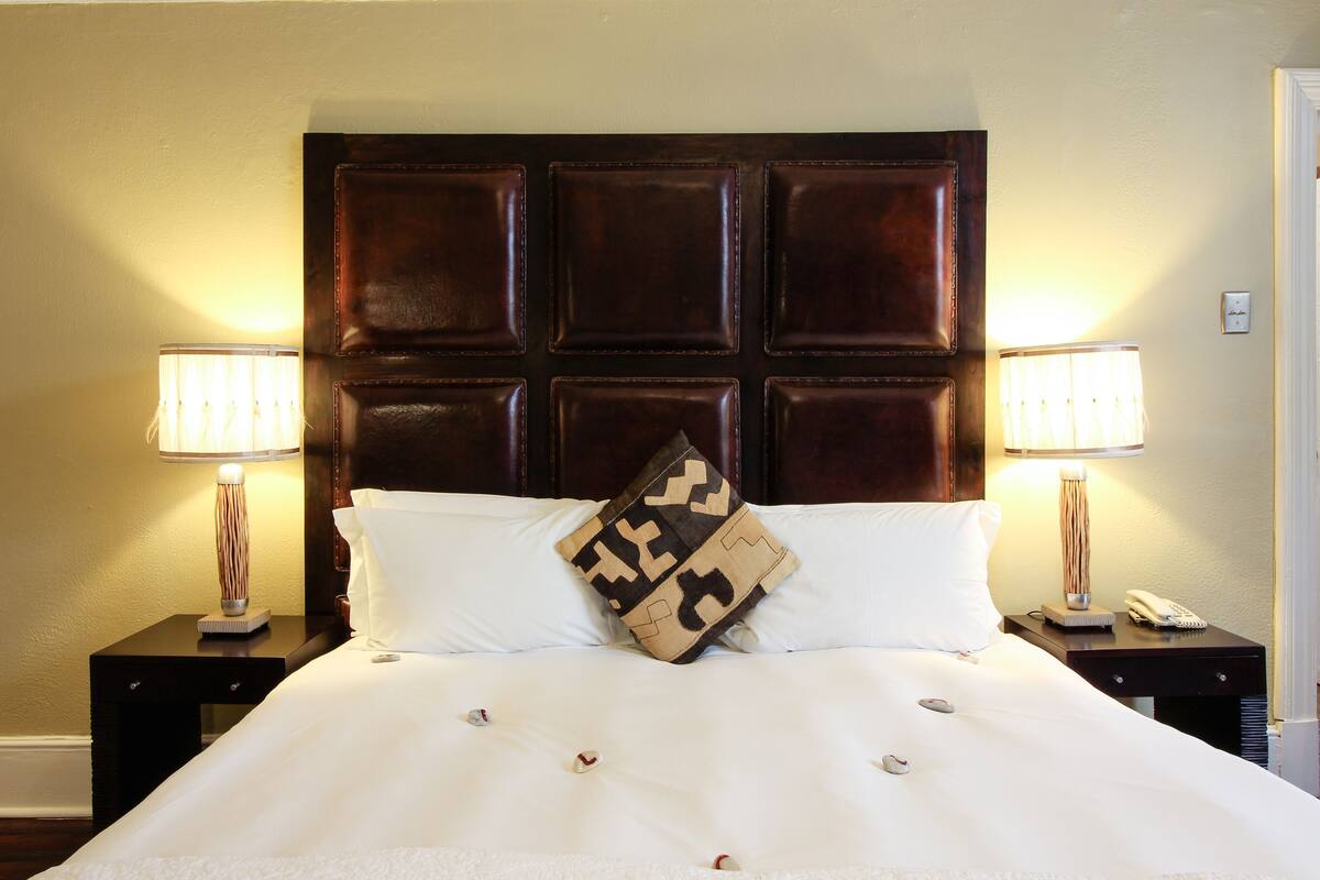 A hotel room with a large bed, two bedside tables, two lamps, a telephone, and a decorative pillow.