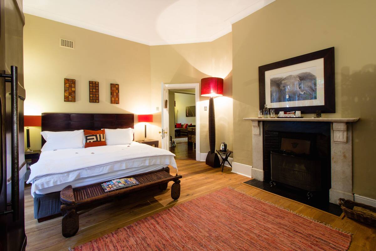 A bedroom with a bed, a fireplace, and a hallway leading to a bathroom.