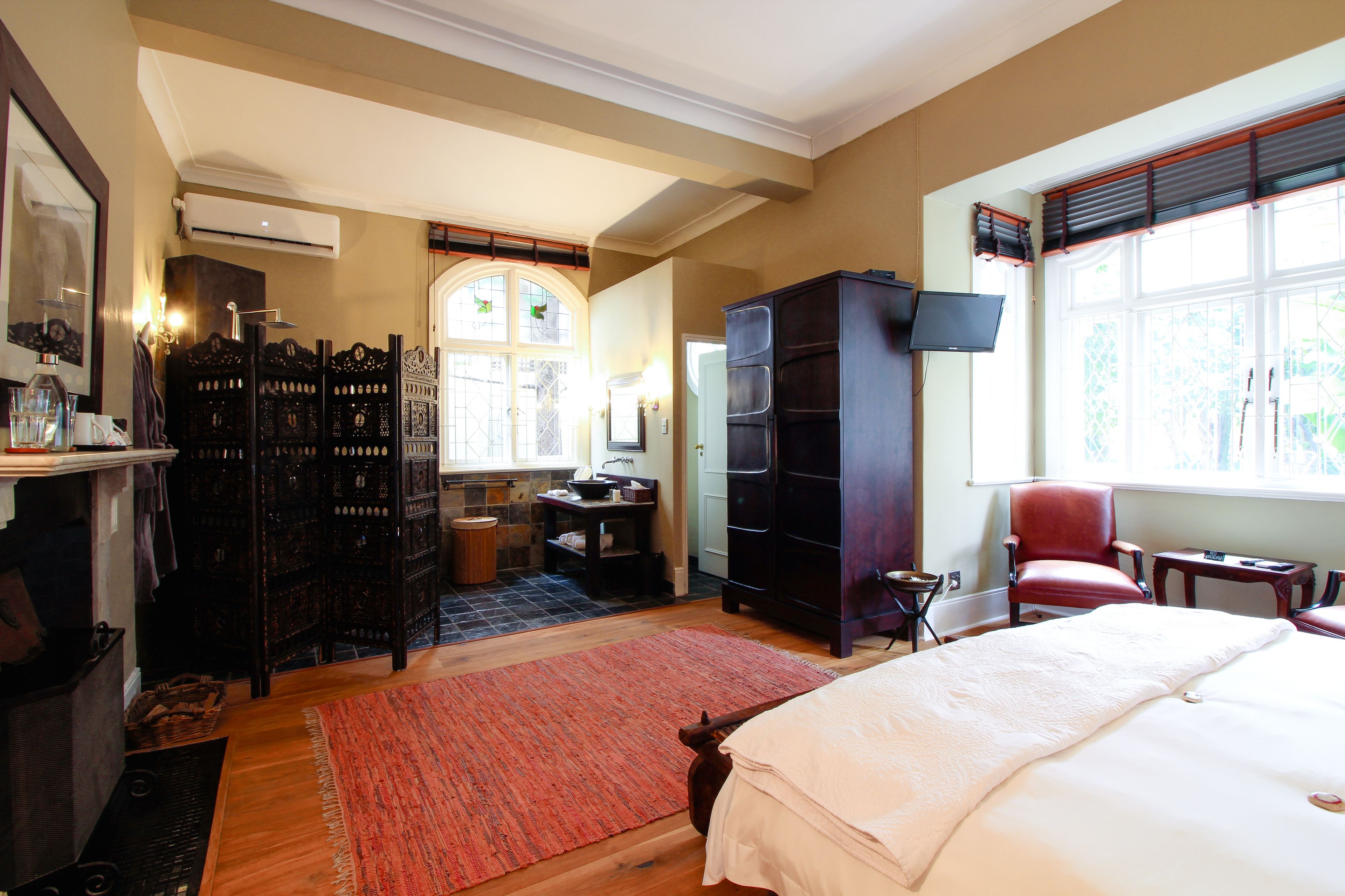Une chambre spacieuse avec un grand lit, un fauteuil rouge, une armoire en bois et un téléviseur.
