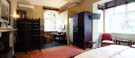 Une chambre spacieuse avec un grand lit, un fauteuil rouge, une armoire en bois et un téléviseur.