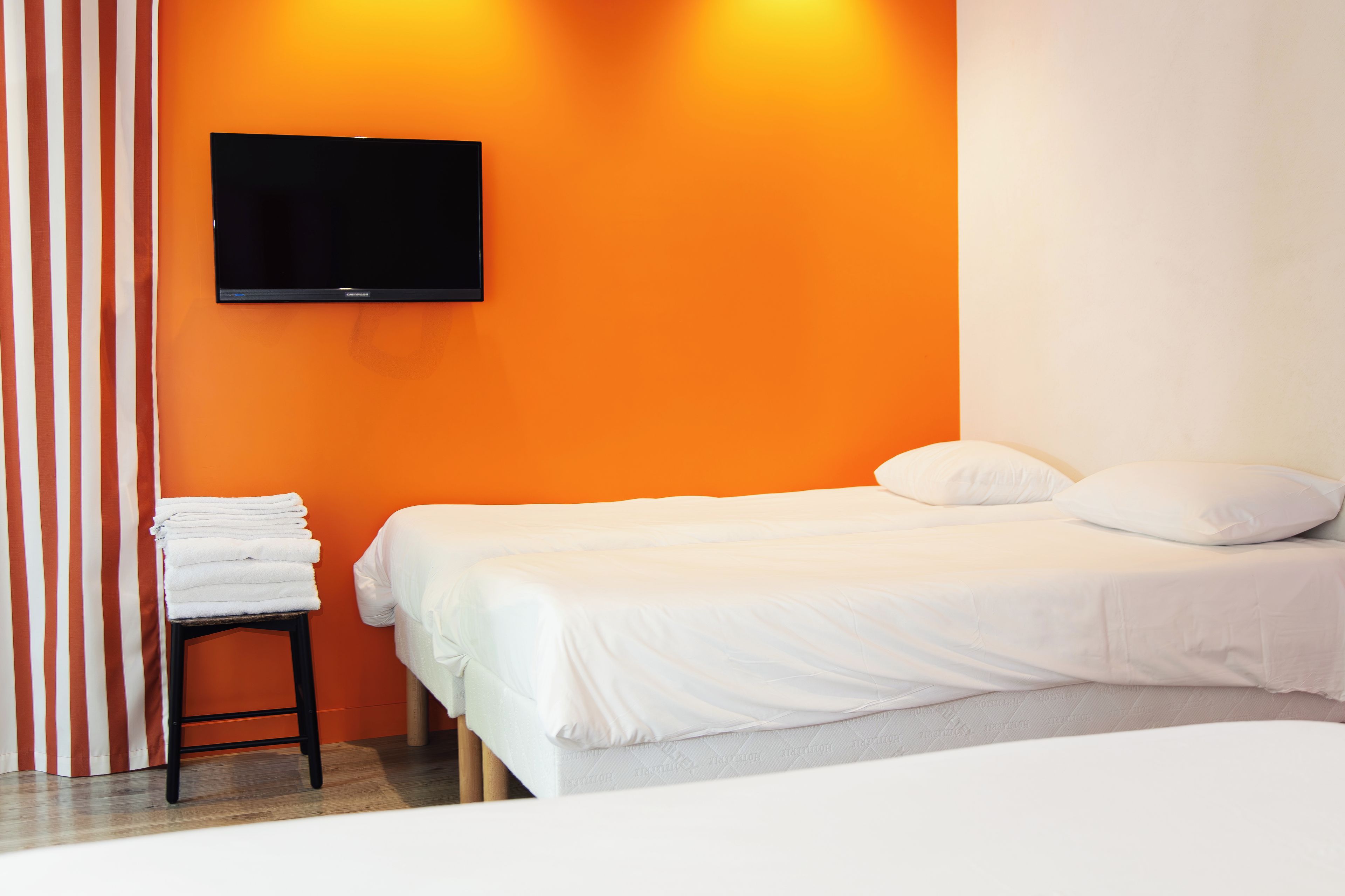 Ein Hotelzimmer mit einem Bett, einem an der Wand befestigten Fernseher und einem Stapel Handtücher auf einem kleinen Tisch.