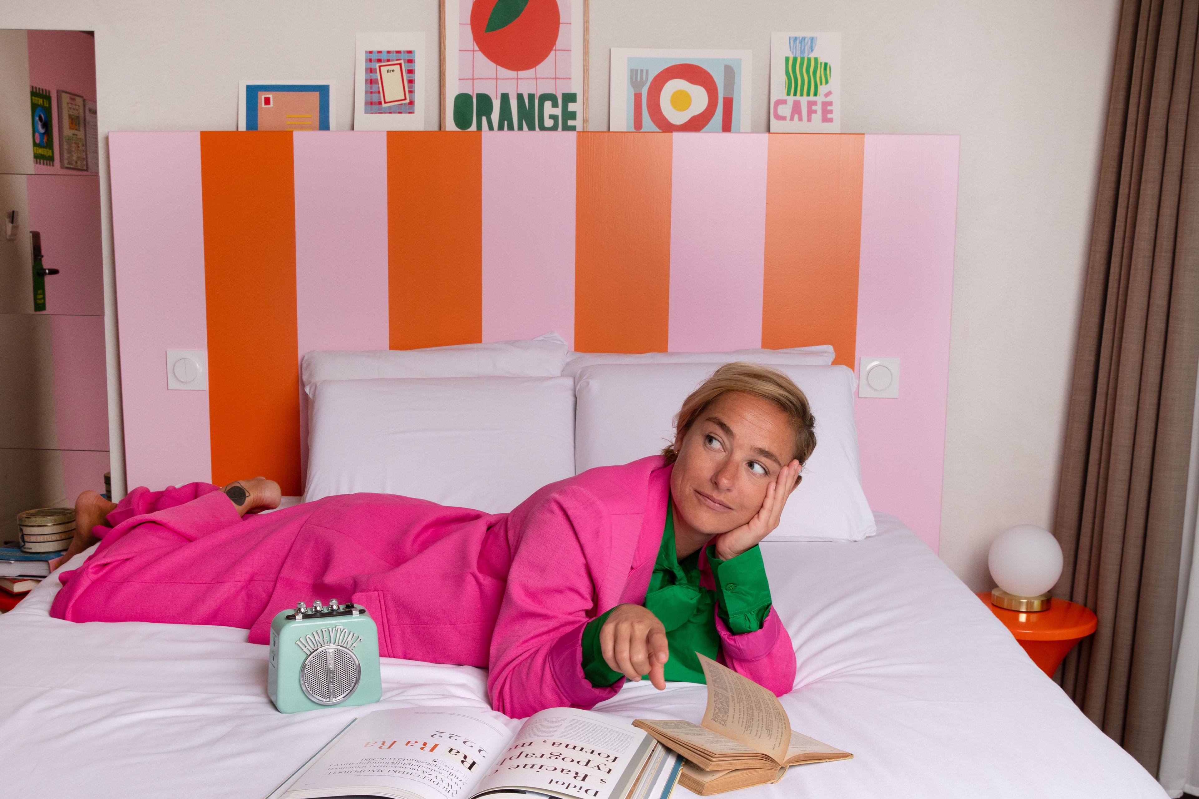 A person lying on a bed with a book, a radio, and a wall with colorful signs.
