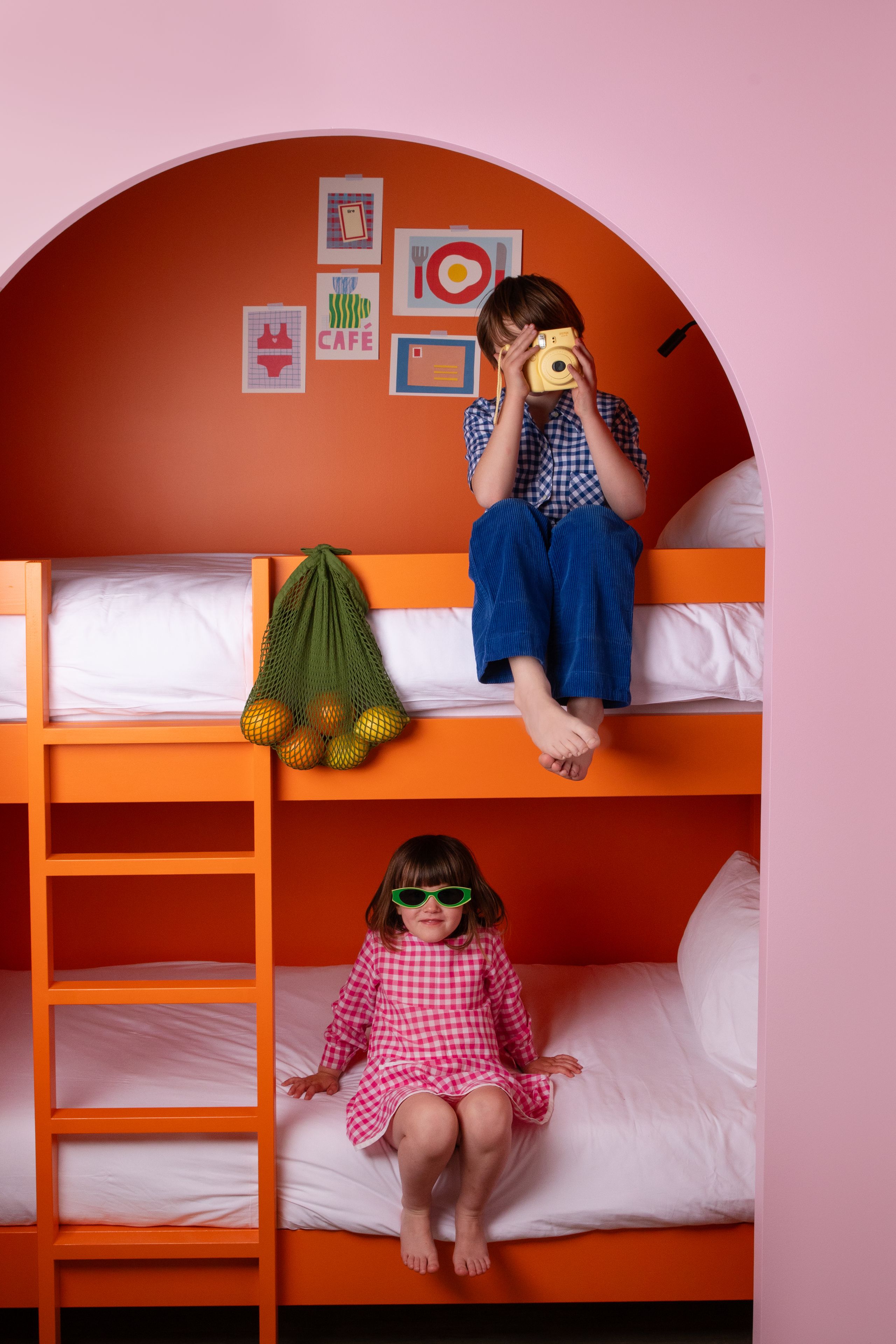 A bunk bed room with orange walls, a ladder, and a hanging net with oranges.