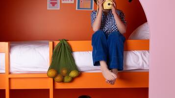 A bunk bed room with orange walls, a ladder, and a hanging net with oranges.