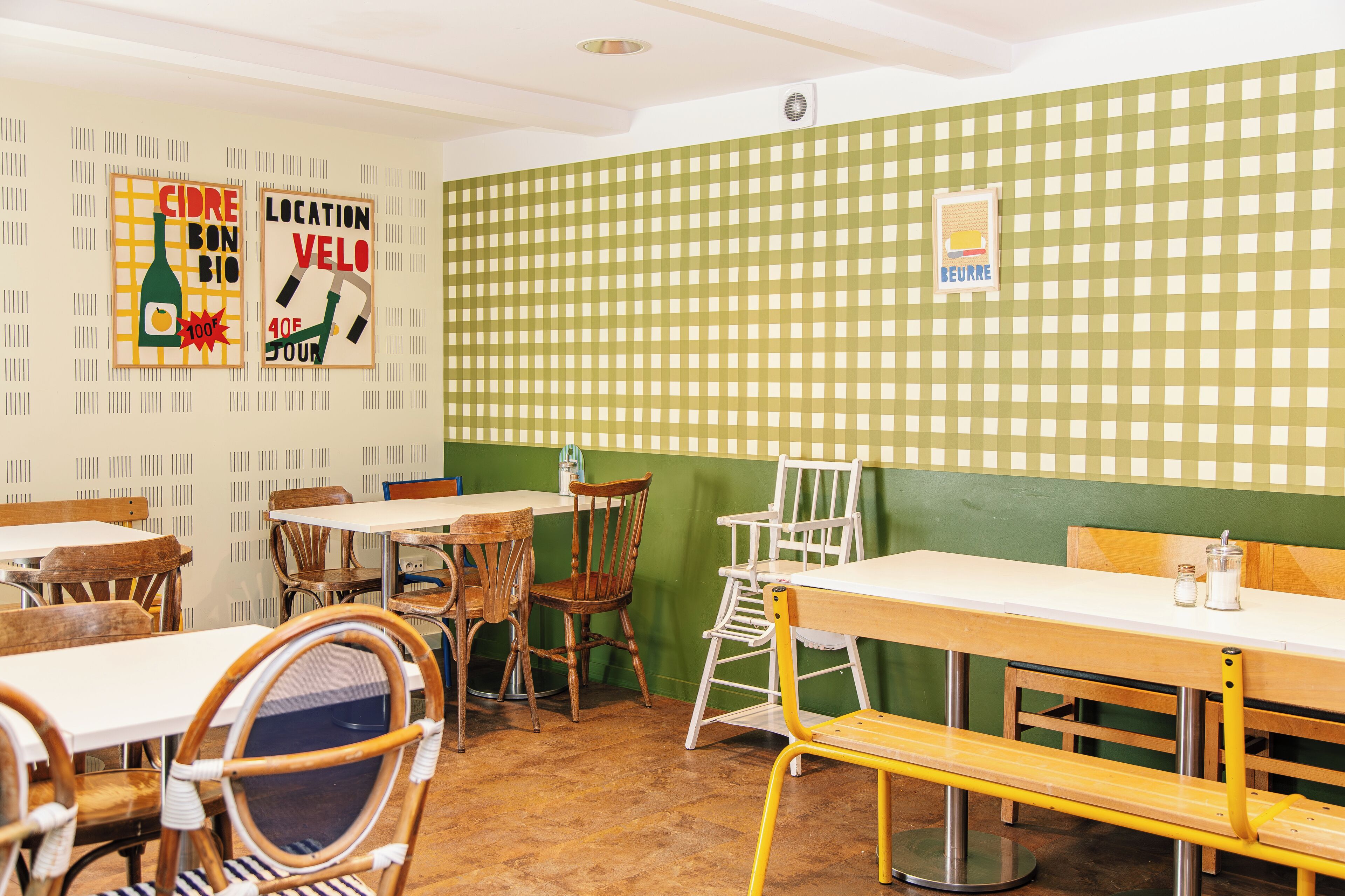 A restaurant interior with wooden tables and chairs, a green checkered wall, and posters on the wall.