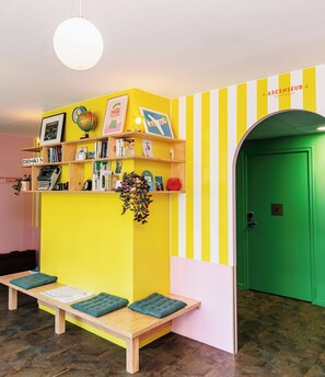 A brightly colored room with a yellow and pink wall, a green elevator, and a wooden bench with cushions. - DEMAIN Hôtel & Conciergerie (Nantes)