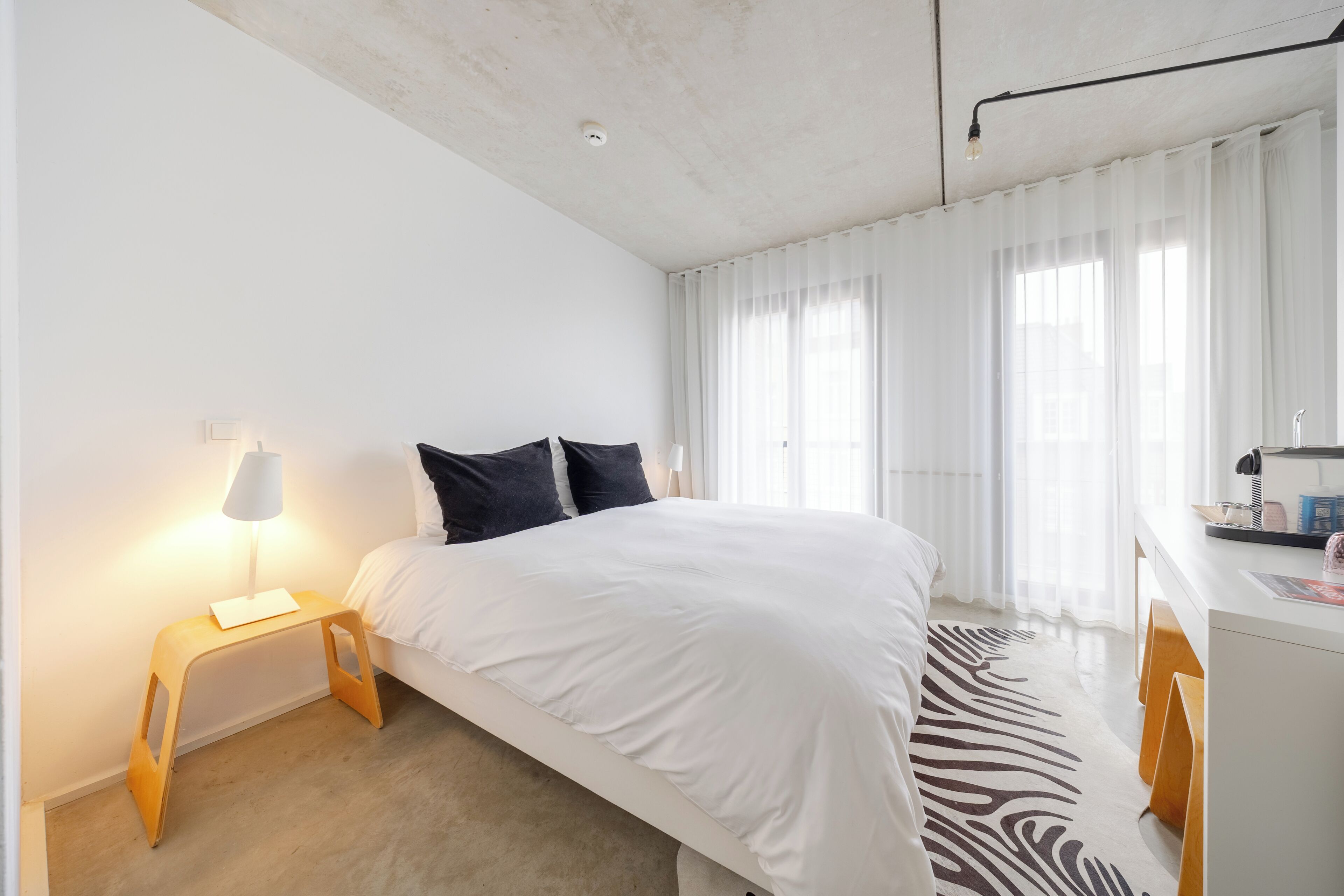 Une chambre moderne avec un grand lit, une table de chevet avec une lampe, un bureau avec une chaise et un tapis à motifs zébrés.