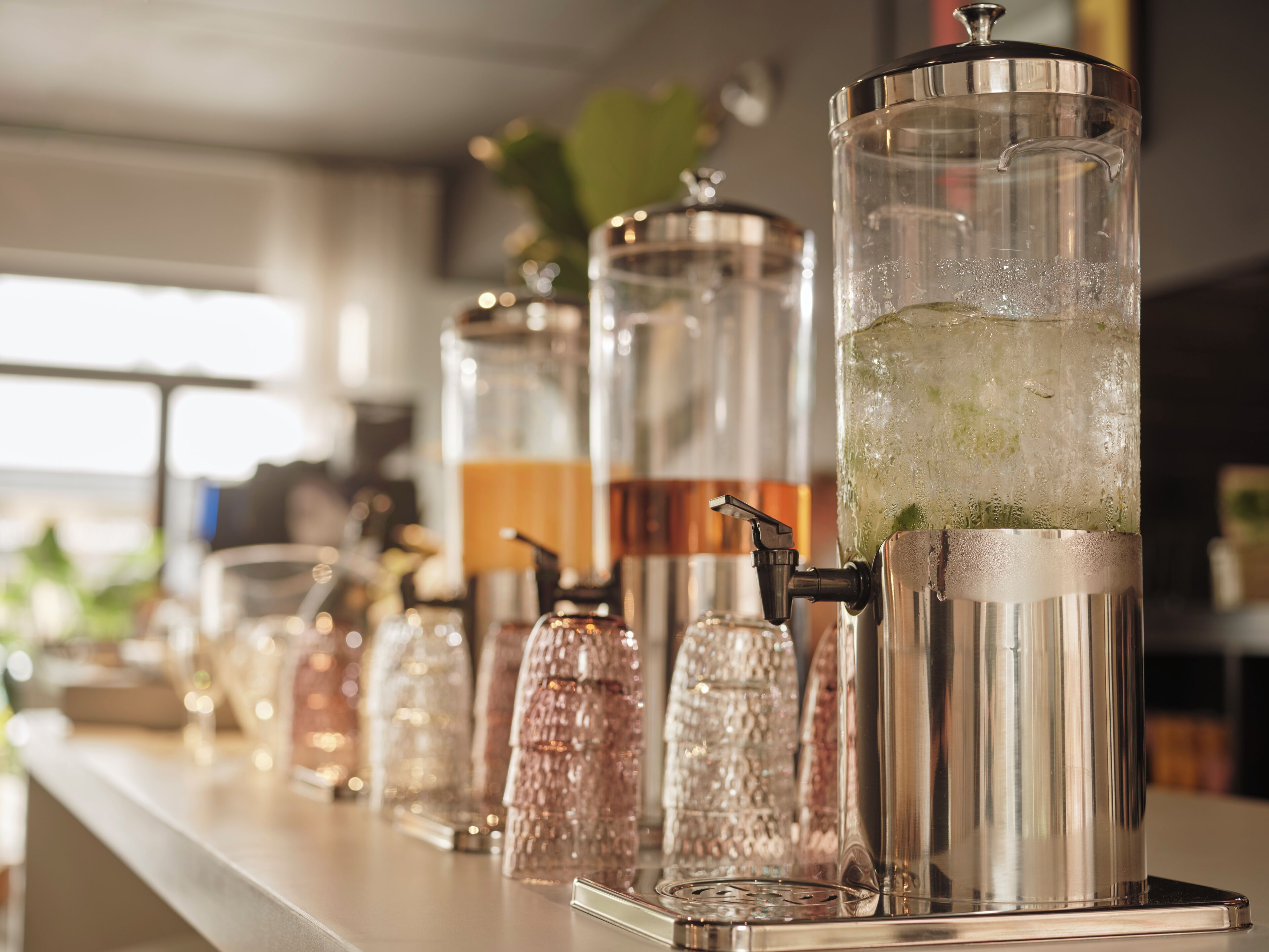 A bar area with a row of beverage dispensers and a large glass container with ice and a drink.