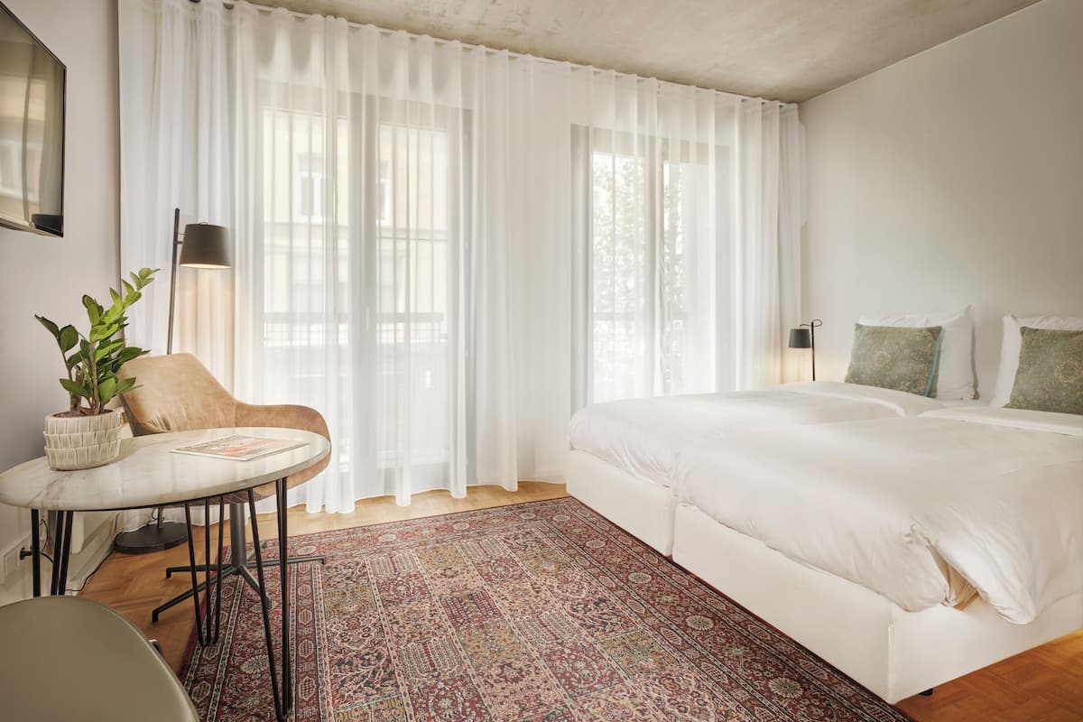 A bedroom with a large bed, a small round table with a plant, and a patterned rug.