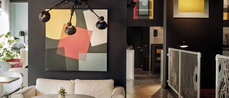 Et moderne interiør med en hvid sofa, et rundt bord og et geometrisk abstrakt maleri på væggen.
