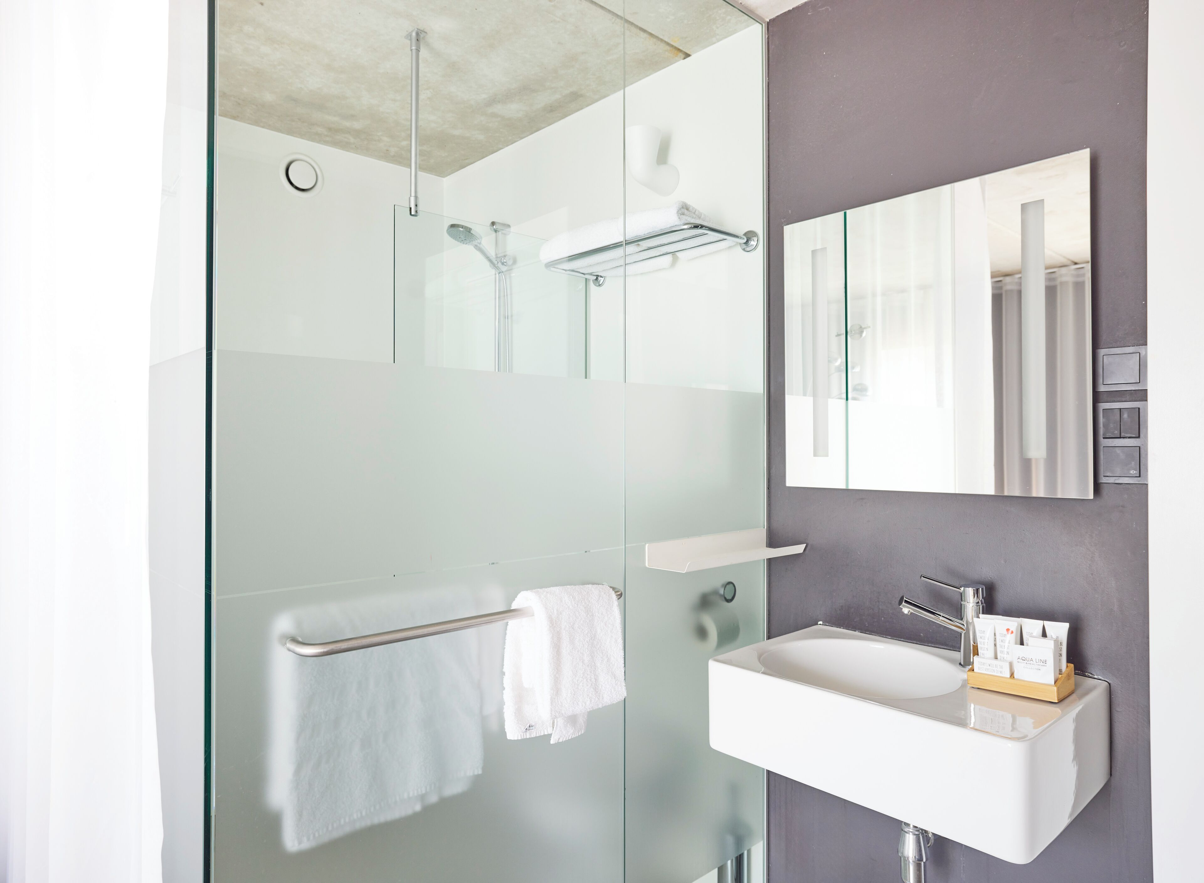 Un baño moderno con ducha de mampara de vidrio, un lavamanos blanco y un espejo grande.