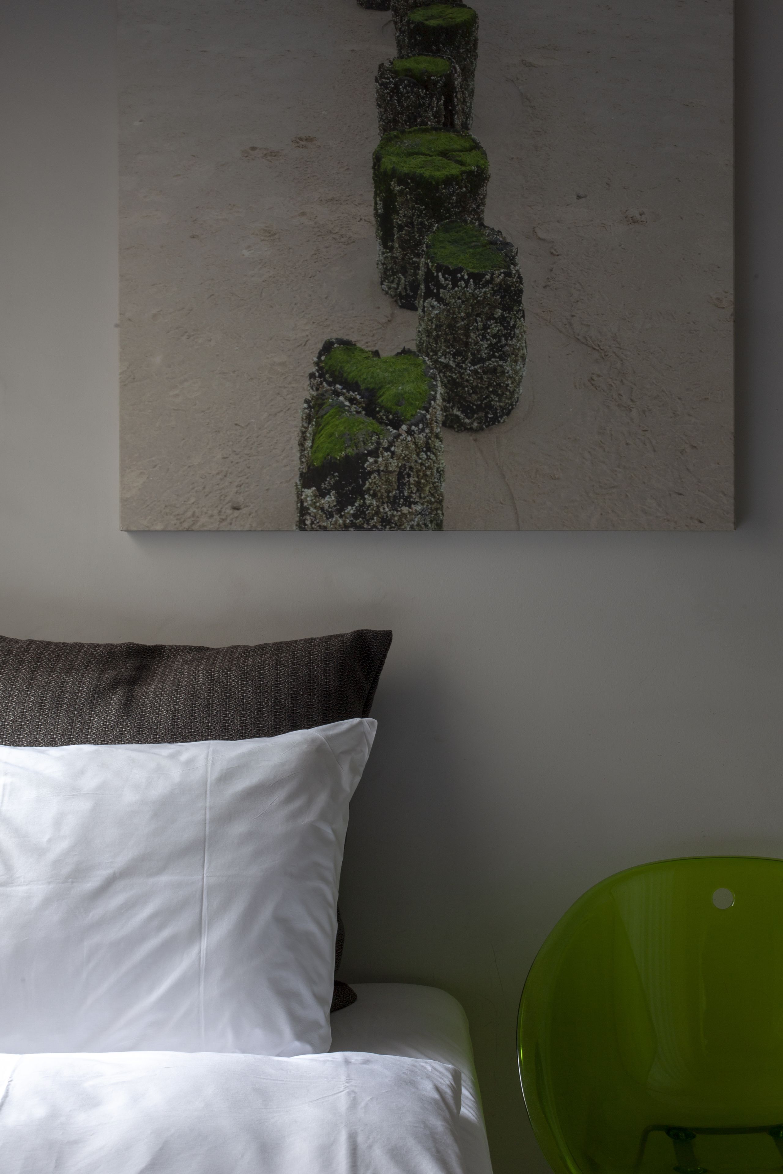Ein Schlafzimmer mit einem Bett, einem grünen Sessel und einem Wandbild mit einer Naturdarstellung.