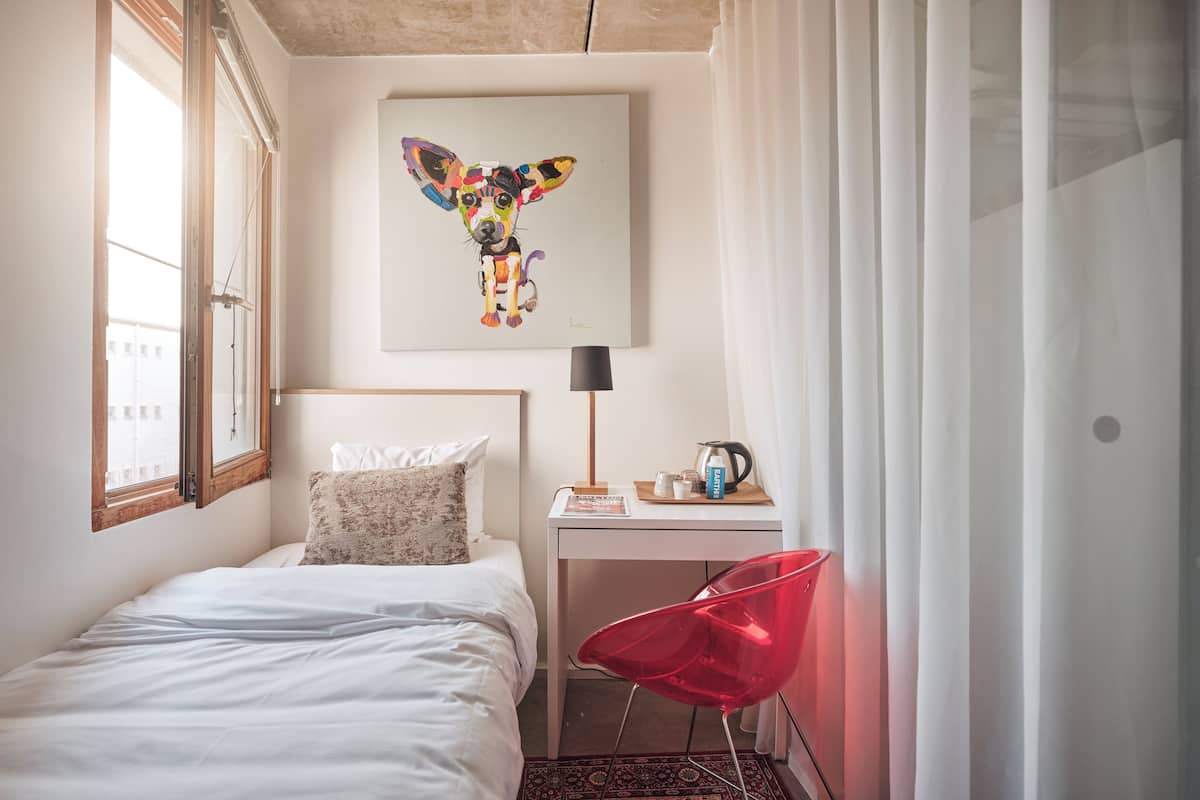 A hotel room with a bed, a desk with a lamp, a chair, and a painting of a dog.