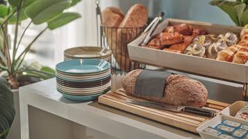 A buffet table with bread, pastries, and a knife on a cutting board.
