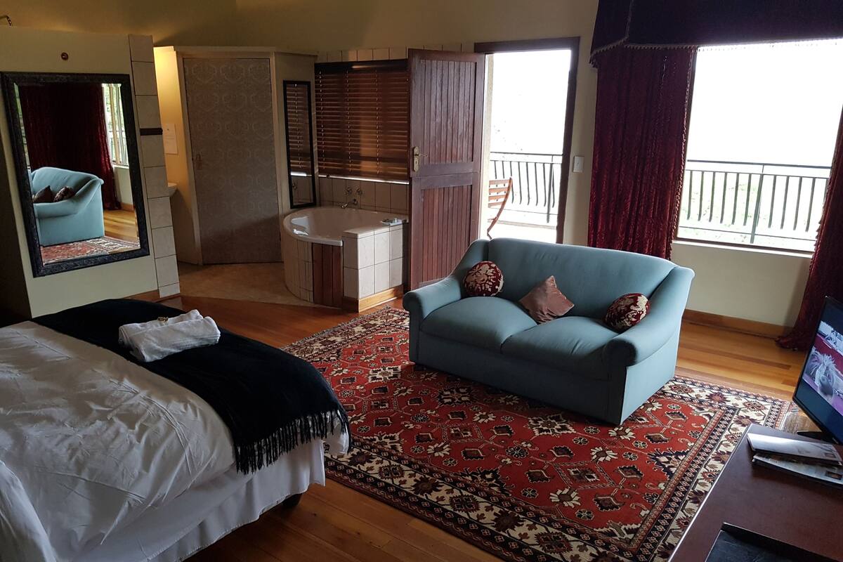 Habitación de hotel con cama, sofá, escritorio, espejo, baño y balcón.
