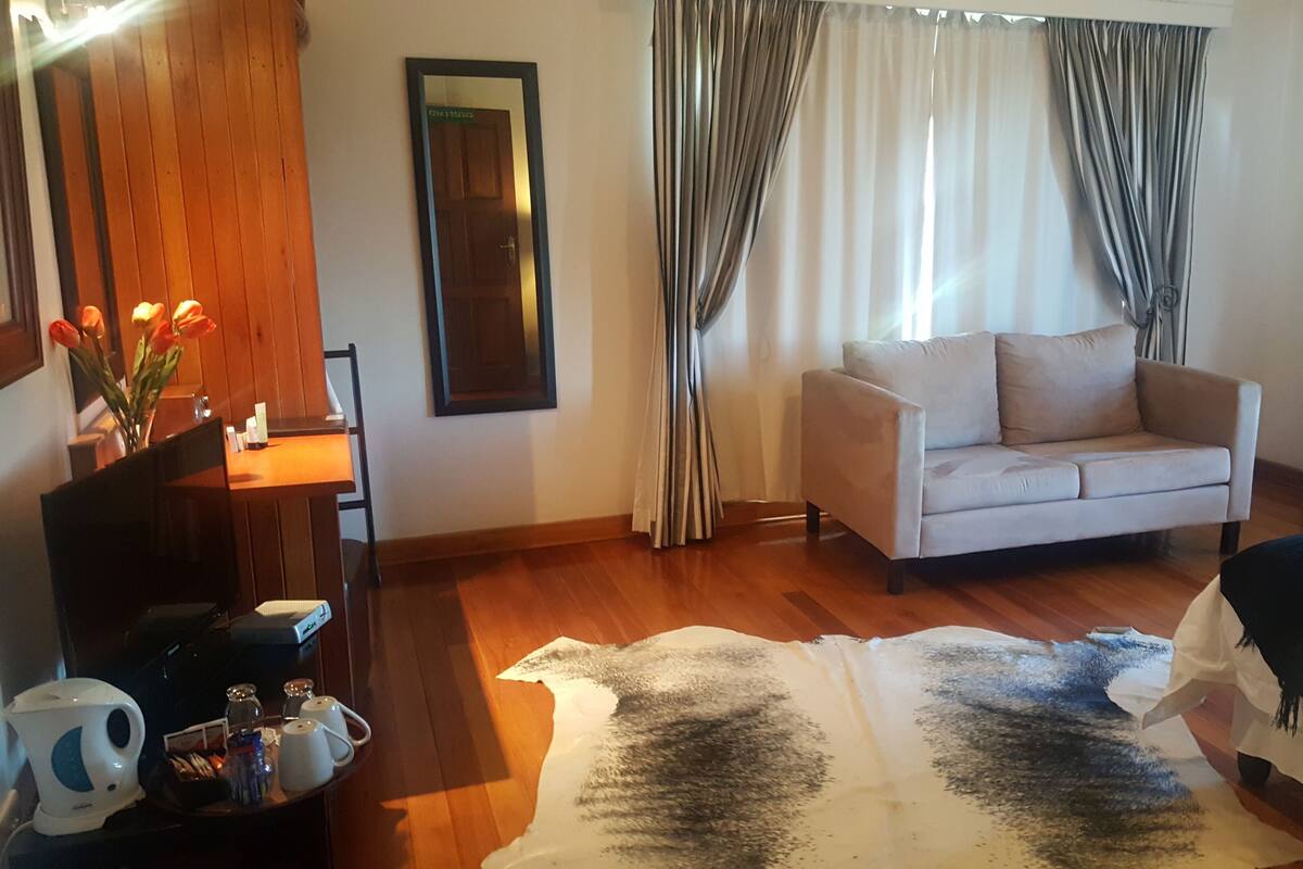 Habitación de hotel con piso de madera, un sofá, una cama, una mesita de centro con una tetera y un espejo en la pared.