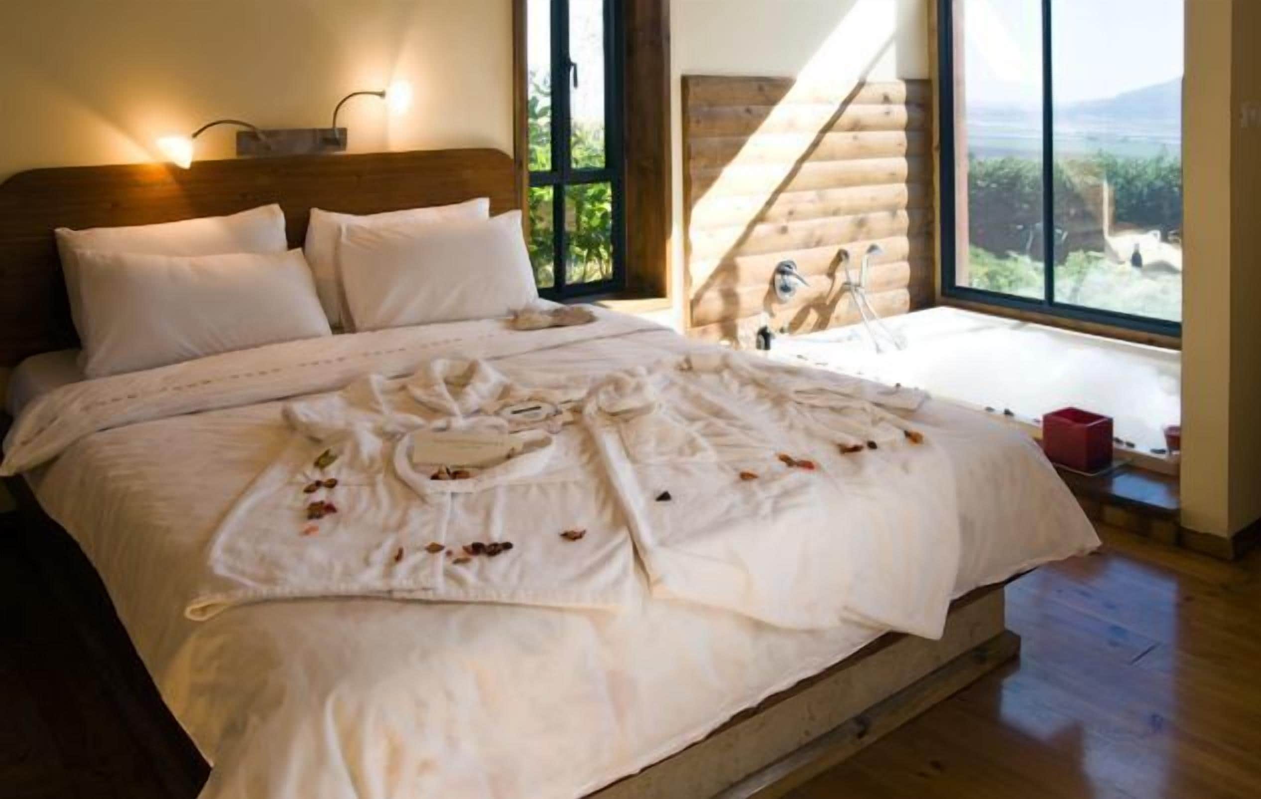 Un grand lit avec du linge de lit blanc et une vue sur un chalet en bois, visible à travers une grande fenêtre.
