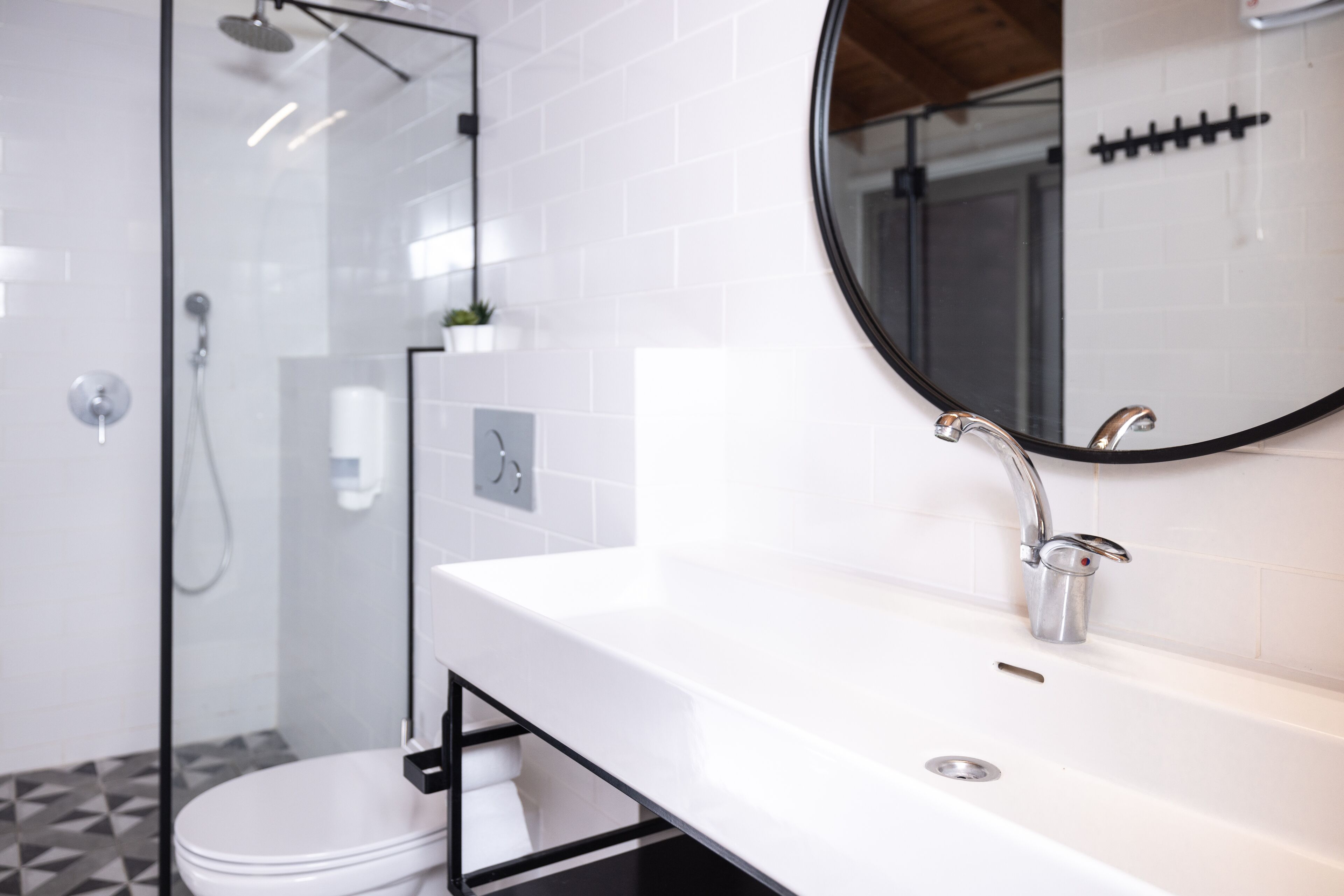 Un baño moderno con un lavamanos blanco, un espejo redondo y una ducha con cerramiento de vidrio.