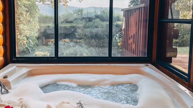 Un bain à remous avec vue sur un jardin et des arbres, grâce à de grandes fenêtres.