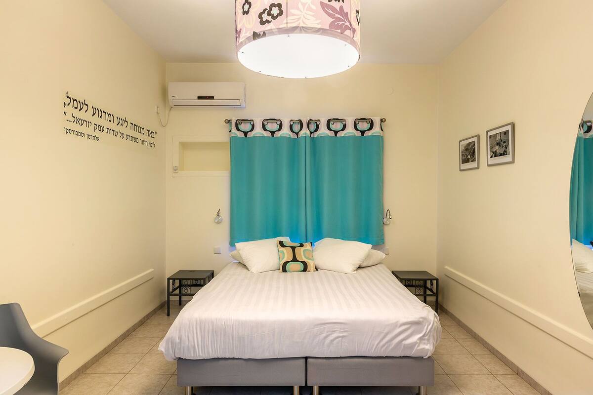 Une chambre à coucher comprenant un lit, une chaise, une petite table, un climatiseur fixé au mur et un luminaire au plafond.