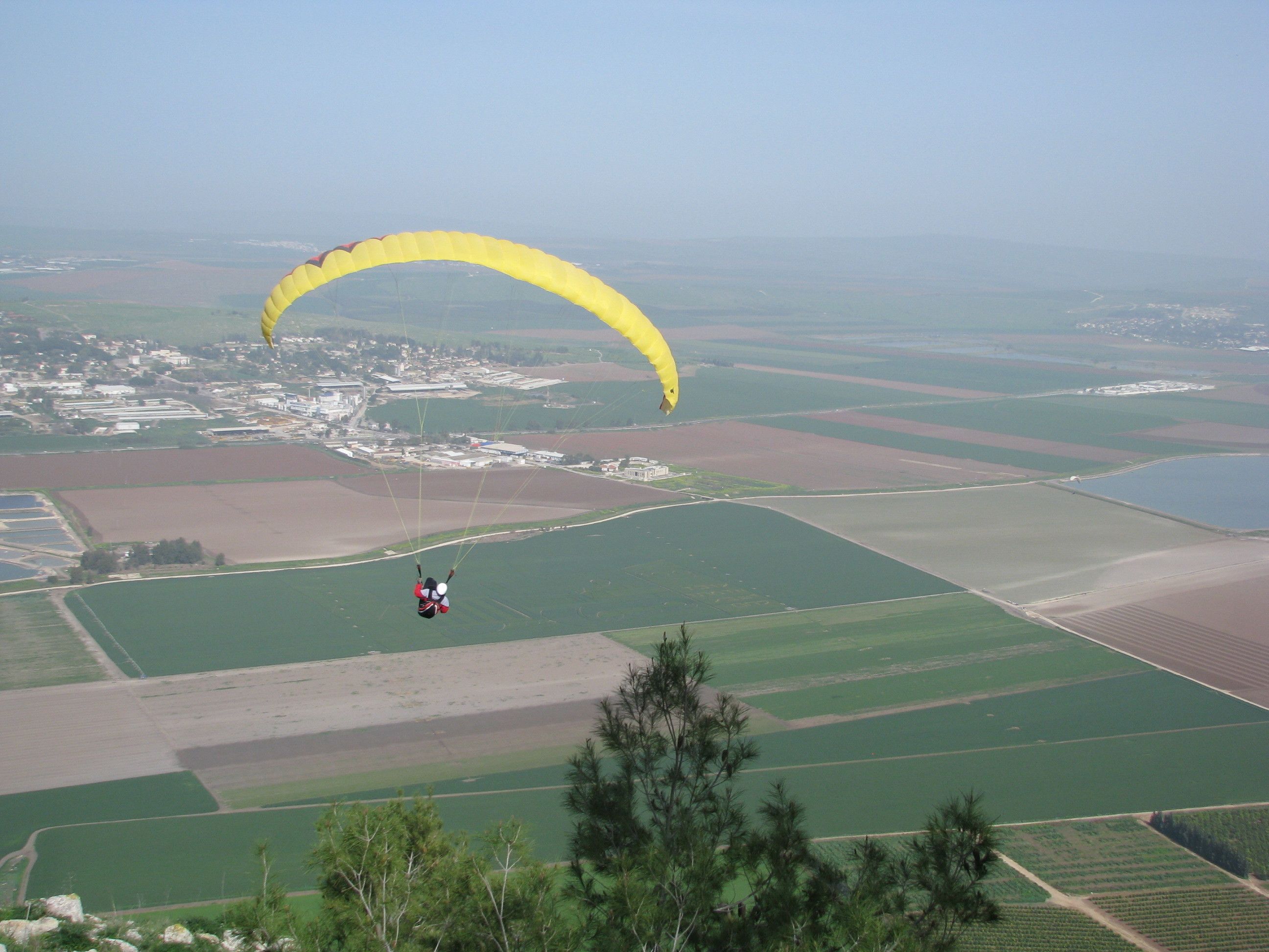 Eine Person macht Gleitflug über eine ländliche Landschaft mit Feldern und einer kleinen Stadt im Hintergrund.