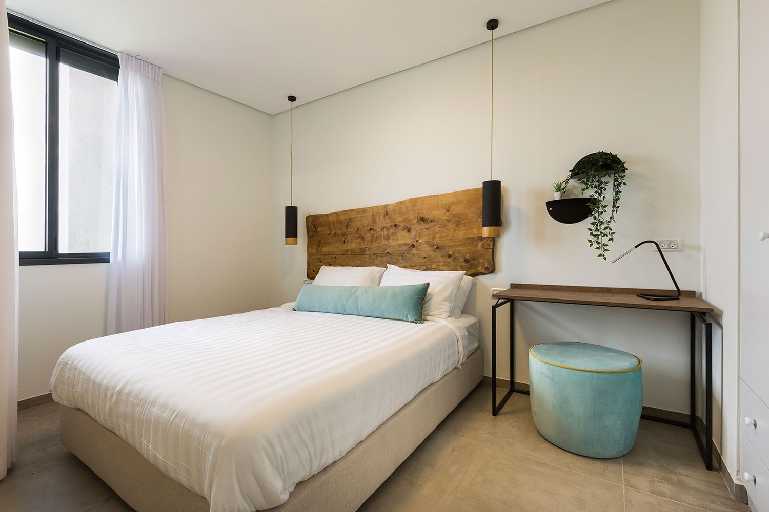 Une chambre à coucher avec un lit, une table de chevet avec une lampe, une plante suspendue et une poubelle.