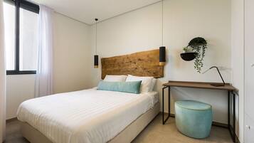 Une chambre à coucher avec un lit, une table de chevet avec une lampe, une plante suspendue et une poubelle.