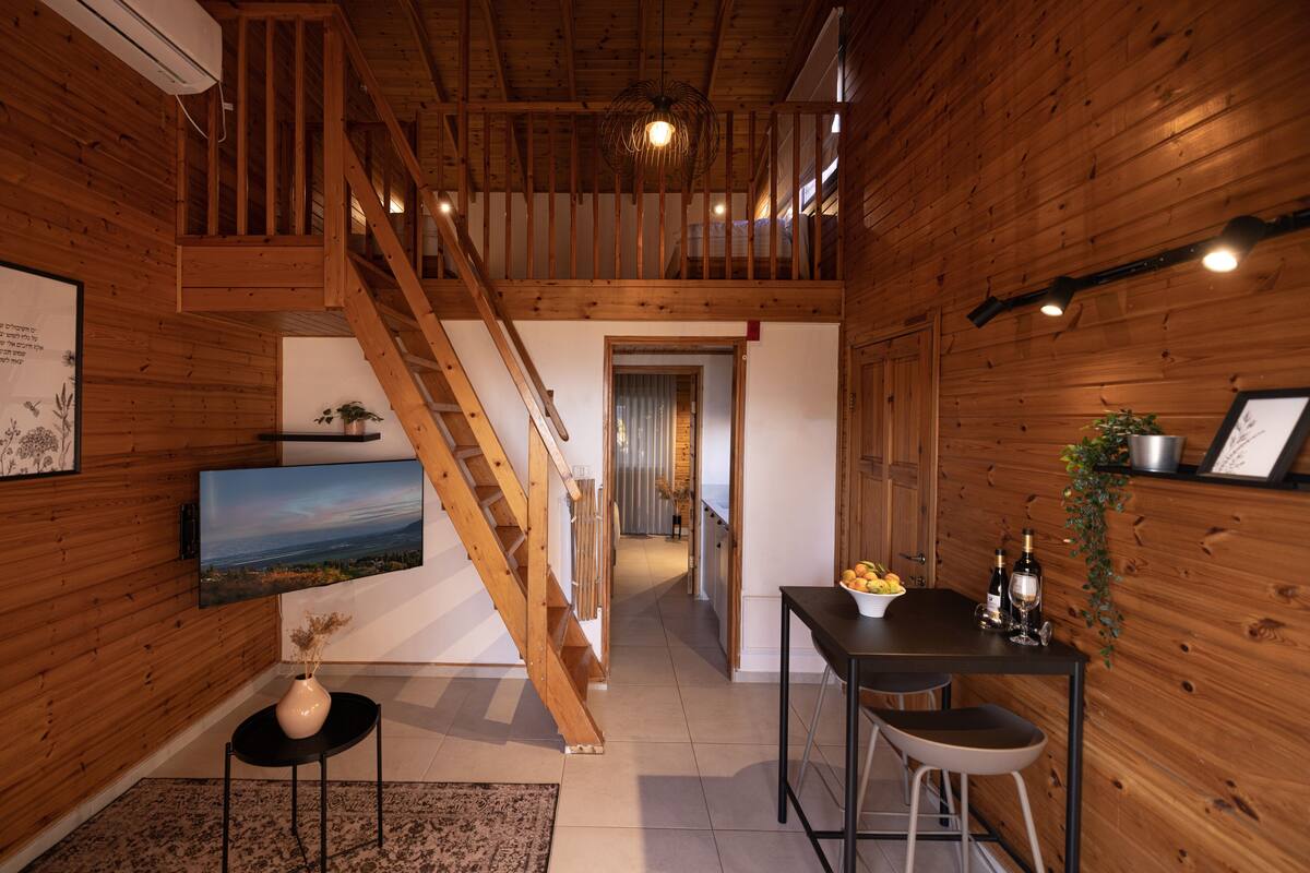 Un intérieur en bois avec un escalier, un coin repas comprenant une table et des chaises, et un téléviseur fixé au mur.