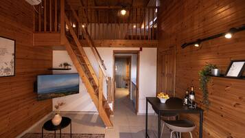 A wooden interior with a staircase, a dining area with a table and chairs, and a television on the wall.