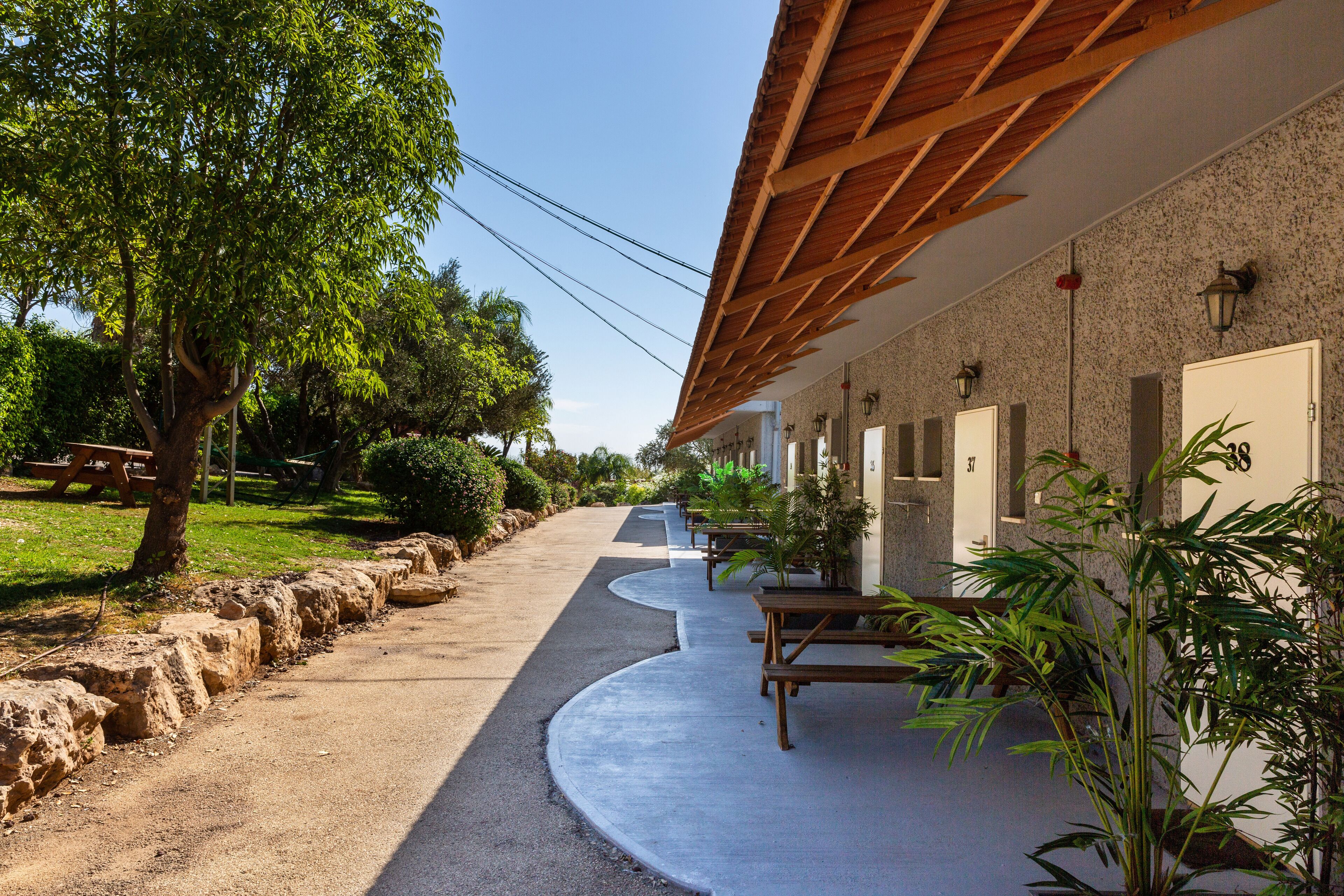 A pathway leading to a building with a covered outdoor seating area, stone walls, and a tree-lined path.