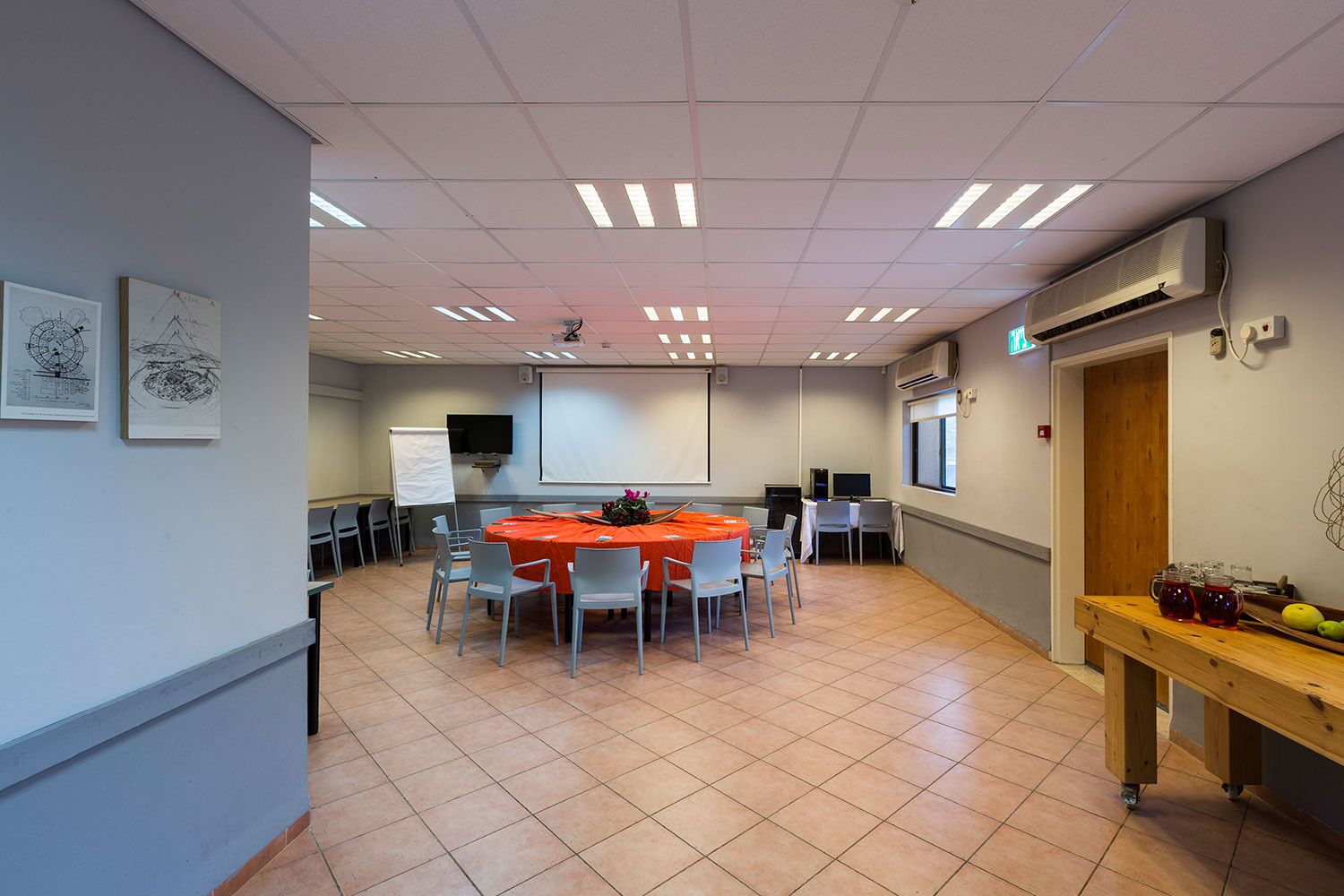 A conference room with a round table, chairs, a projector screen, and a whiteboard.