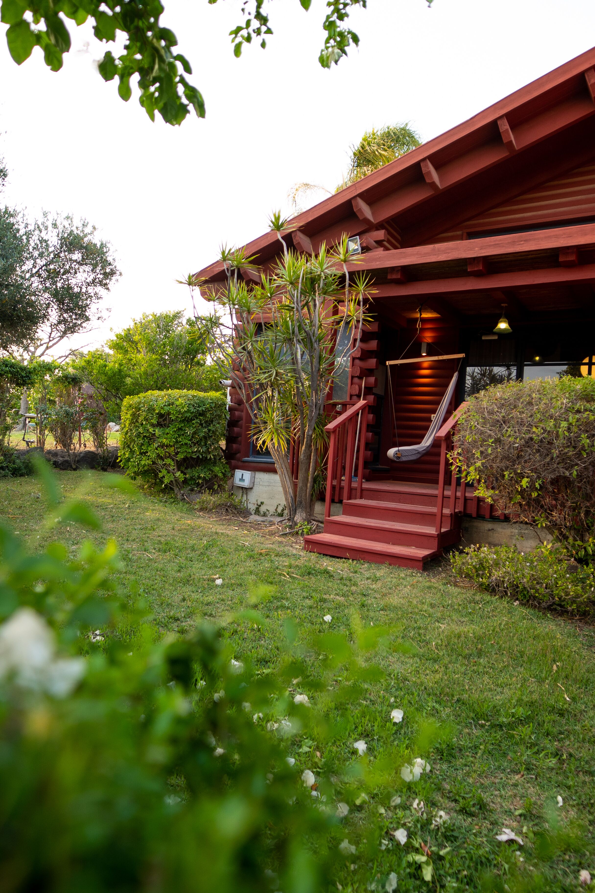 A red wooden building with a staircase leading to a porch, surrounded by greenery.