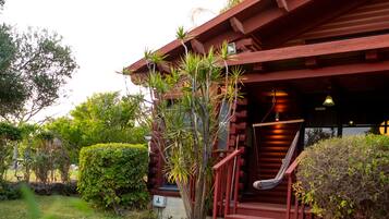 A red wooden building with a staircase leading to a porch, surrounded by greenery.