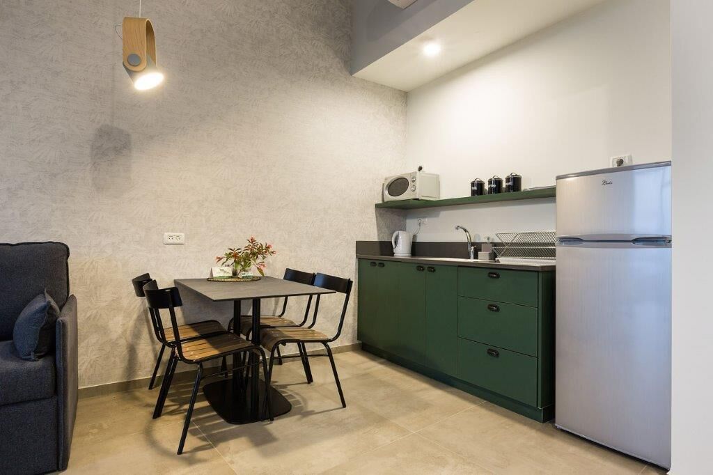 Une cuisine de taille réduite avec un coin repas, des meubles de couleur verte et un réfrigérateur blanc.