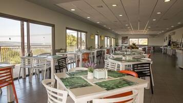 A spacious dining area with multiple tables and chairs, large windows offering views of the outdoors, and a clean, modern interior design.