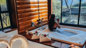Une salle de spa avec une tête de lit en bois, une table de massage et une vue sur les arbres à travers de grandes fenêtres.