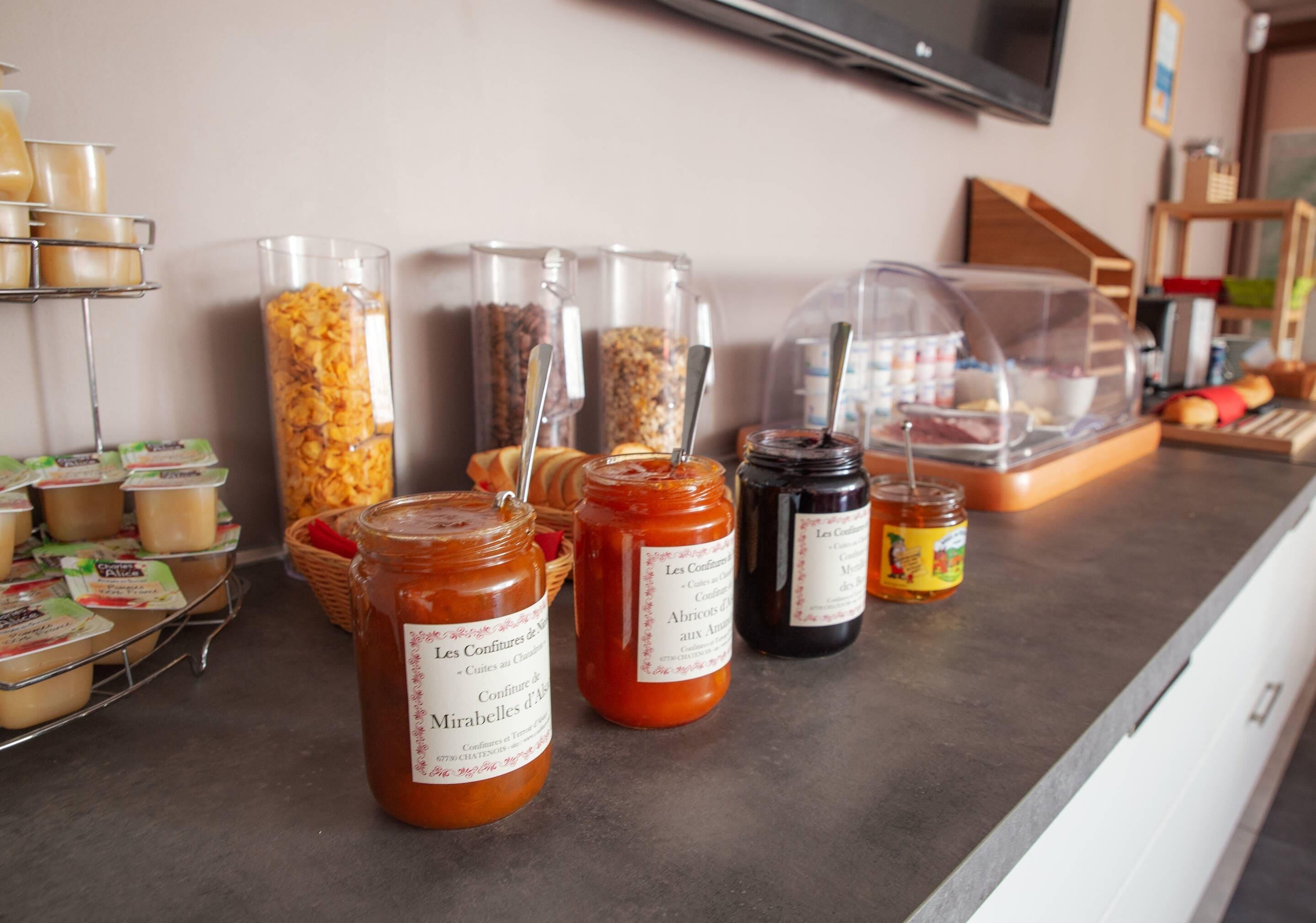 A kitchen counter with various food items and condiments, including jars of honey and jams, and a bread basket.