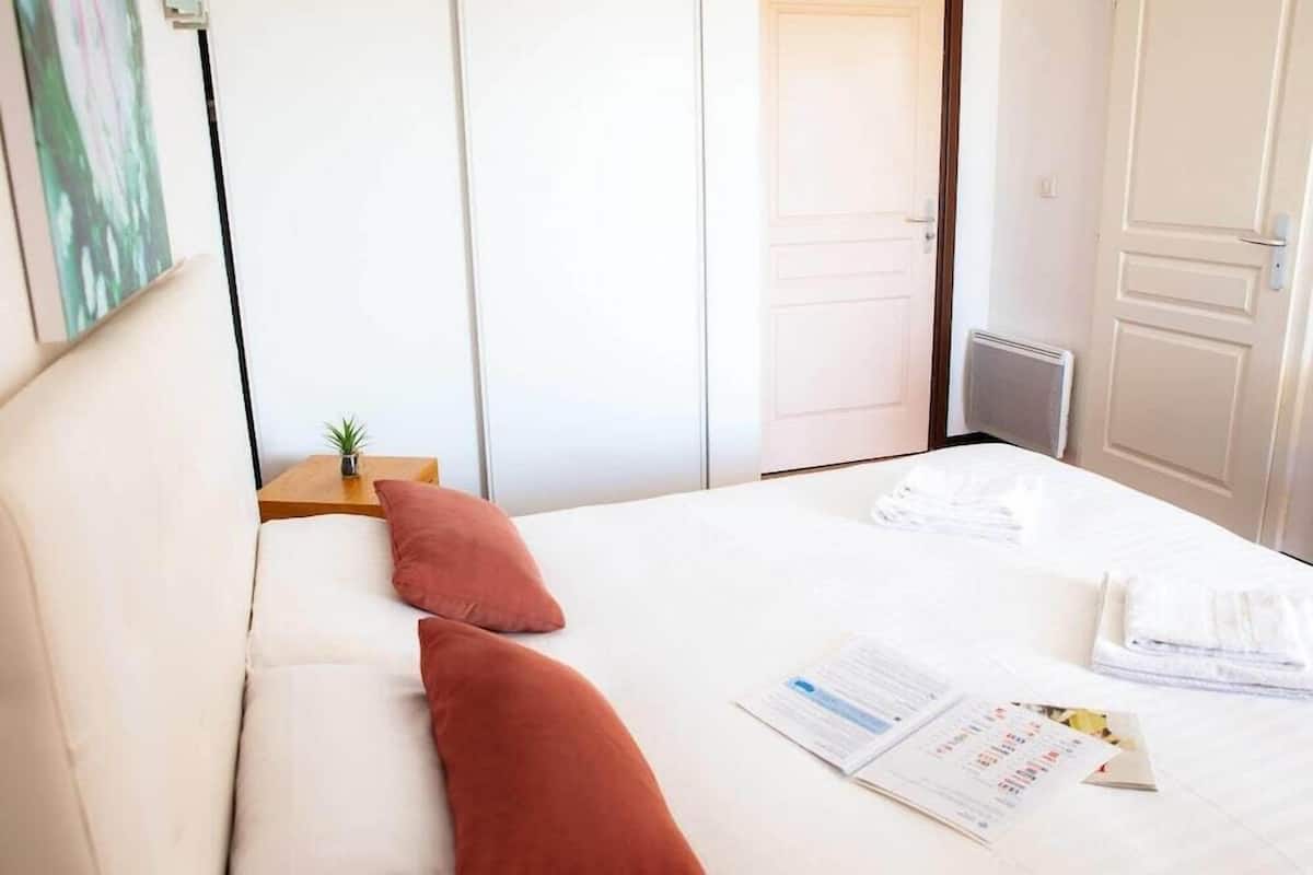 Habitación de hotel con cama, almohadas, una mesita con una planta y una puerta que da a otra habitación.