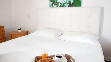 Un lit bien fait, avec du linge de lit blanc, un plateau contenant des éléments de petit-déjeuner, notamment un croissant, un verre de jus d’orange et une tasse de café.