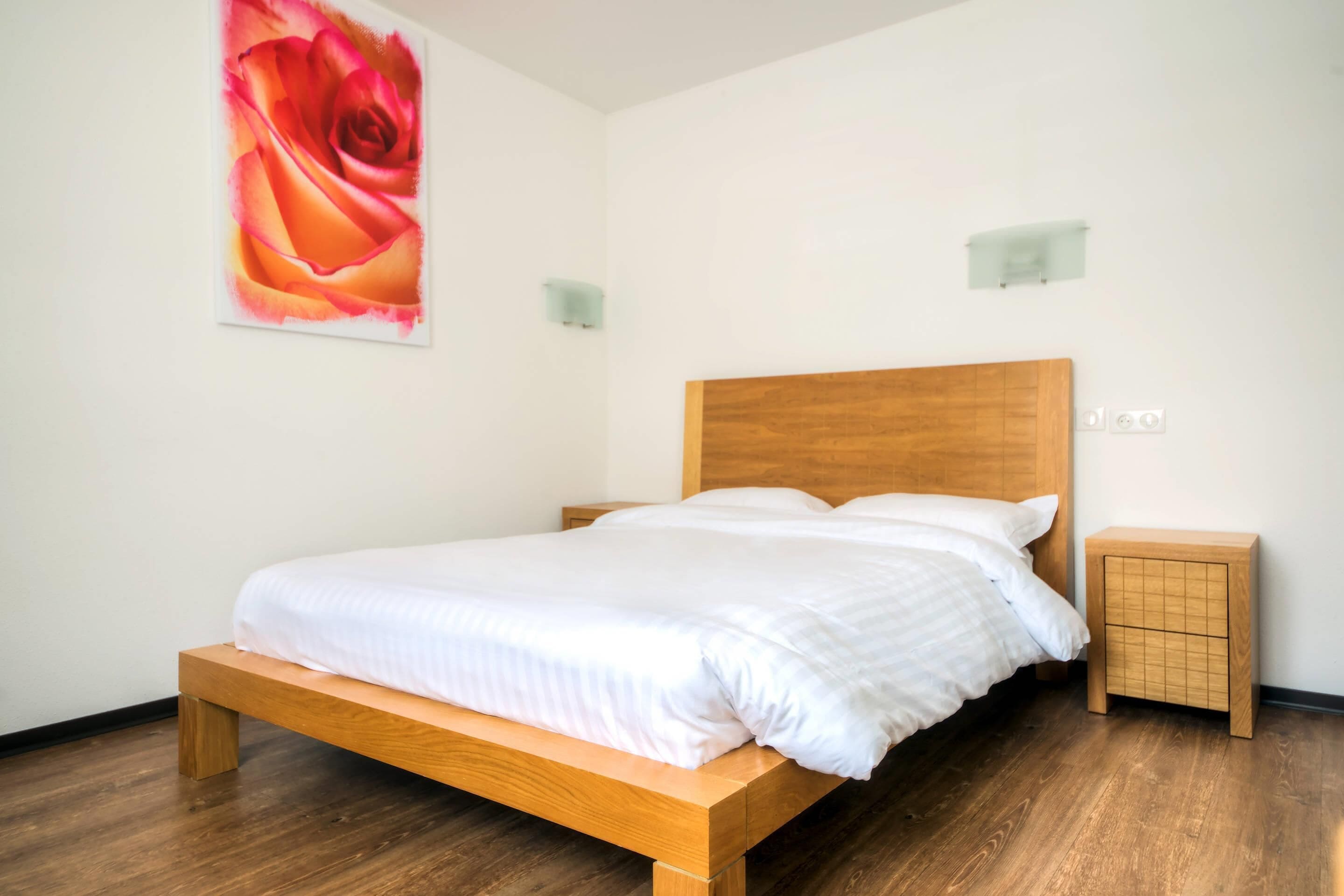 A neatly made bed with a wooden headboard, a small bedside table, and a wall-mounted light fixture.
