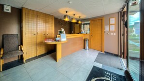 Un espace d’accueil comprenant un comptoir en bois, une chaise d’attente, un bureau de réception et une vue sur l’extérieur grâce à une porte vitrée.