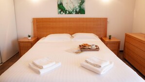 Una cama bien hecha con toallas dobladas, una bandeja con croissants y café, y un cuadro de una rosa en la pared.