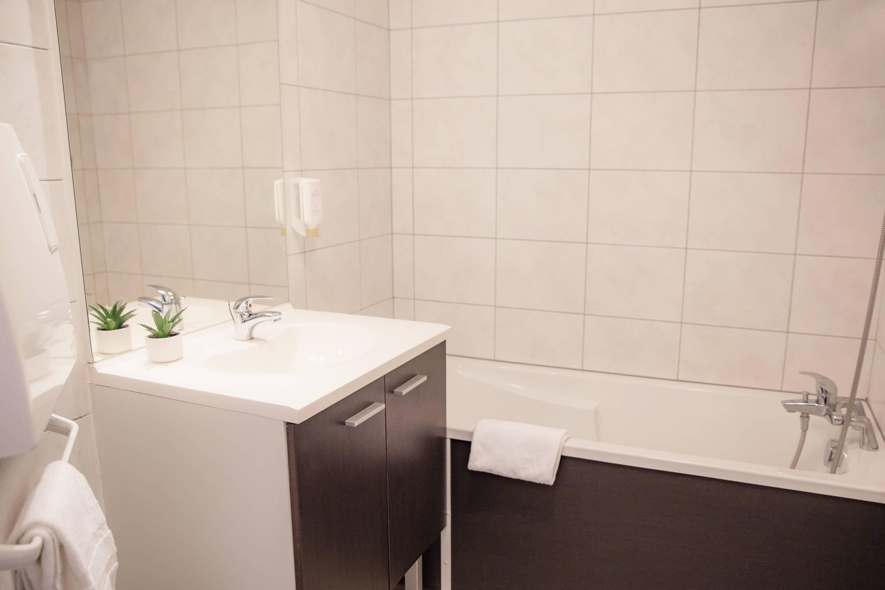 Une salle de bain moderne avec un lavabo blanc, des meubles sombres, une baignoire et une serviette accrochée au mur.