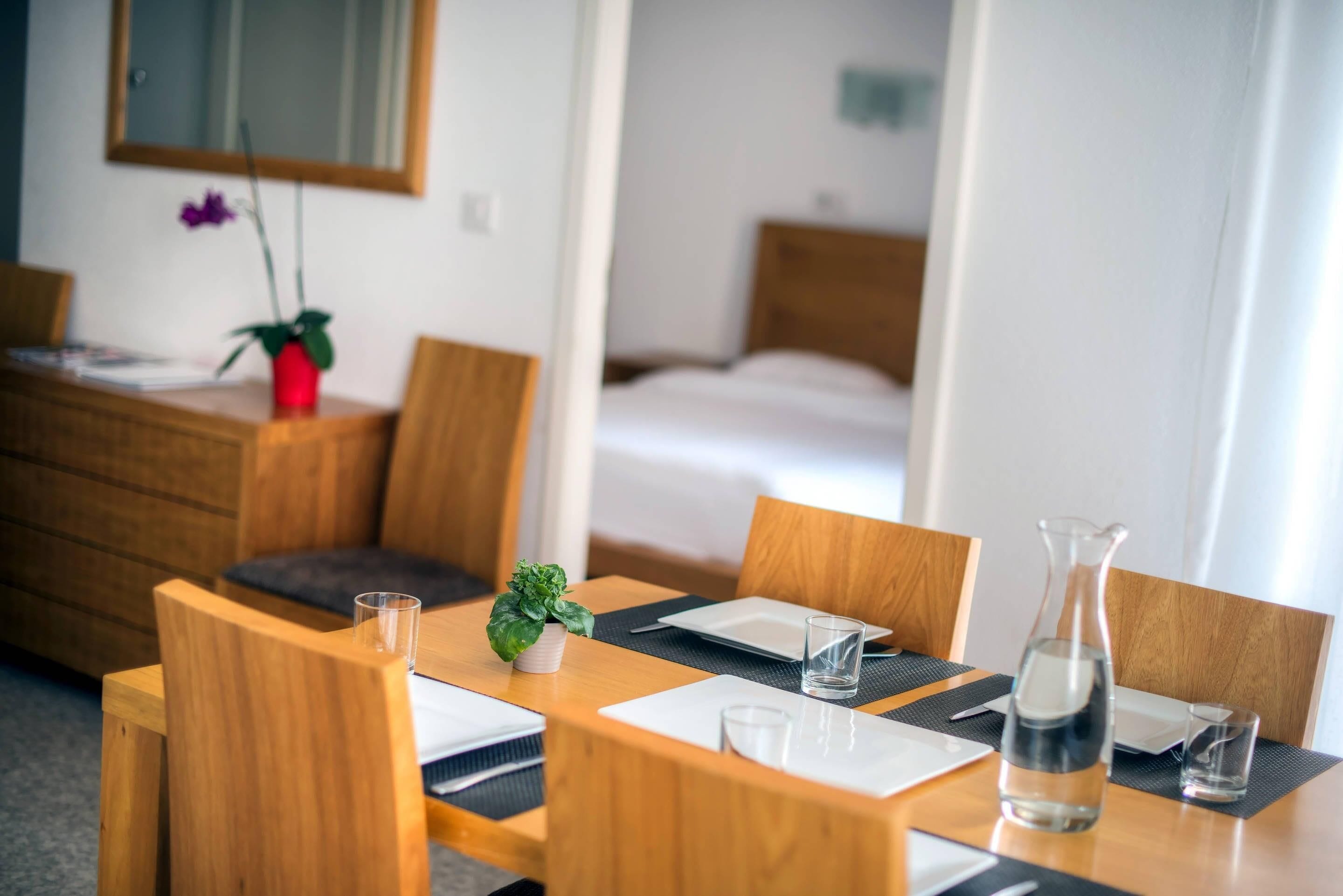 Ein Hotelzimmer mit einem Holztisch für zwei Personen, einem Bett im Hintergrund und einem kleinen Blumentopf auf dem Tisch.